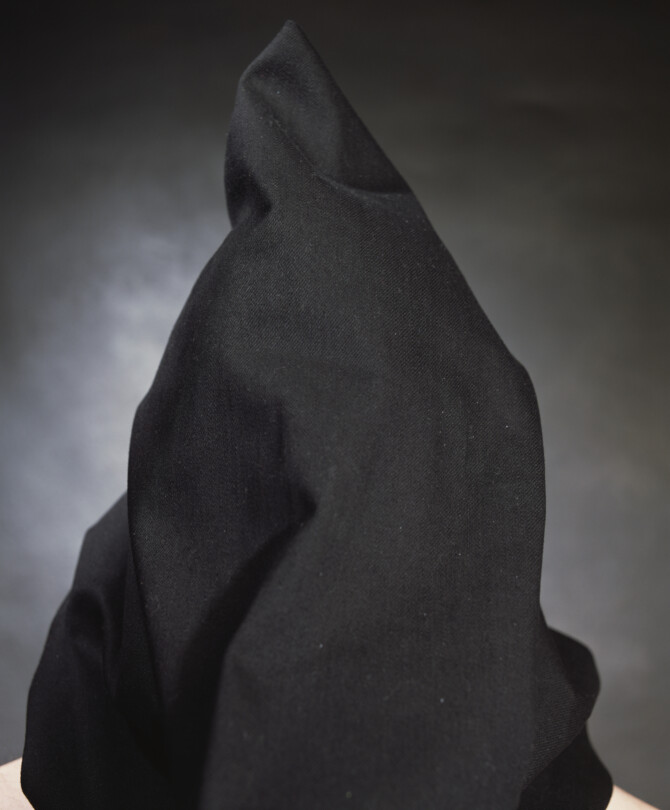 Photo by artist Andres Serrano titled 'Francie McGiugan, "The Hooded Men"'. It features a black hooded figure with bare shoulders, stood against a grey background.