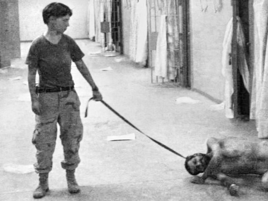 Real image from Abu Ghraib prison in which a female US soldier is pulling a naked inmate across the floor by a belt tied around his neck.