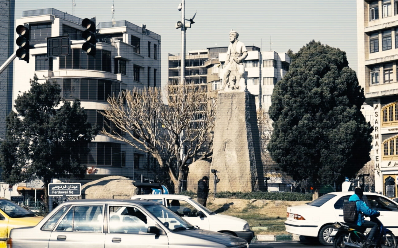 Screenshot from the trailer for Alamut by Laibach. The picture depicts a busy roundabout featuring a sculpture of an important figure in the centre.